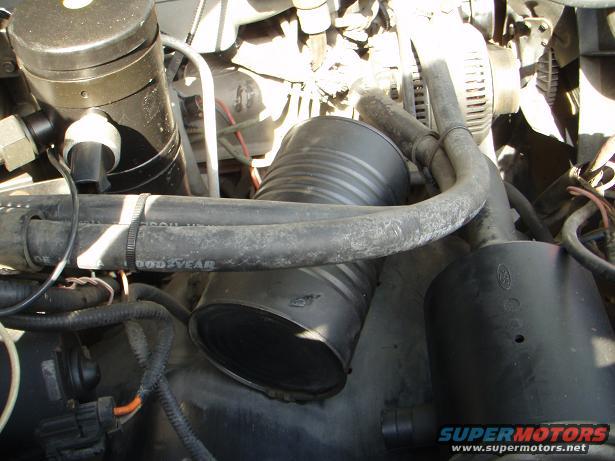 Engine bay showing a large black air intake hose and other engine components. Text 'GOODYEAR' is visible on a hose