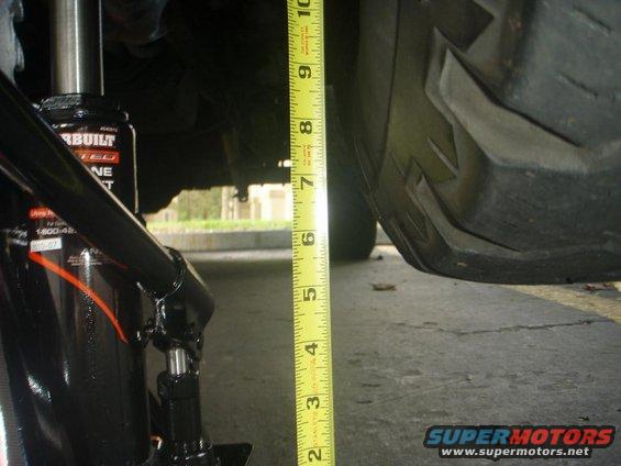 Measuring ground clearance next to a tire with a tape measure and a jack