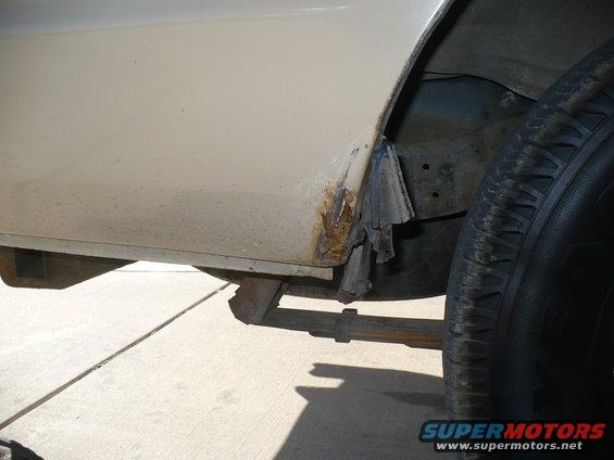 Cream-colored vehicle's lower rear quarter panel showing significant rust damage and a black tire