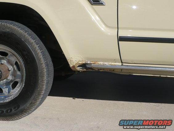 Close-up of a tan vehicle's side, showing rust on the rocker panel below the door and wheel well