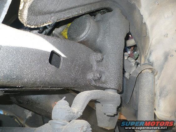Close-up of greasy vehicle suspension parts, including a tie rod end and steering knuckle, with a Supermotors.net watermark