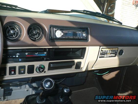Vehicle dashboard with Panasonic stereo, climate controls, and gear shifters. Brown and tan interior