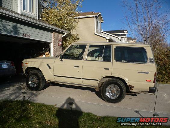 Tan Toyota Land Cruiser parked in driveway, side view, showing rust on rear quarter panel