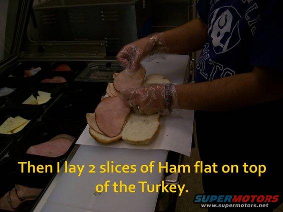 Person in blue shirt and gloves layering ham on bread at a sandwich counter