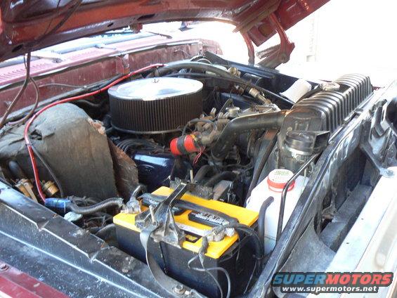 1978 Ford Bronco engine bay with a large air filter, yellow battery, and red hoses