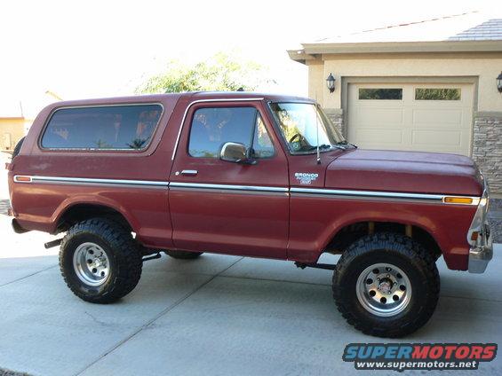Red 1978 Ford Bronco with chrome trim and aftermarket wheels parked in front of a garage