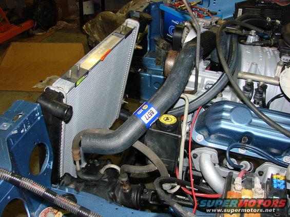 Blue Jeep engine bay showing a radiator, hoses, and engine components. A blue label with '8677' is visible on a hose