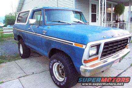 Blue 1978 Ford Bronco with white top, chrome grille, and white-rimmed wheels parked on a concrete driveway