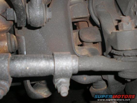 Close-up of a vehicle's steering linkage and suspension parts, showing metal rods and bolts