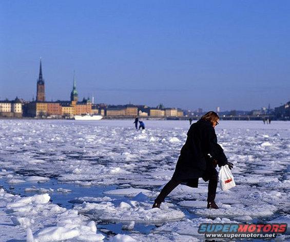 People walk on a frozen body of water with a city skyline and a ship in the distance