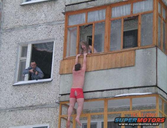 Man hanging from balcony, being pulled up by a woman, another man watches from window