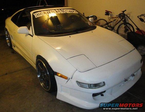 1991 Toyota MR2, white, with a black t-top roof and a banner reading "HIDE YOUR DAUGHTERS" on the windshield