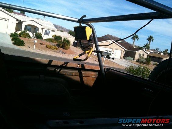 Interior view of a vehicle with roll cage, looking at a white SUV on a suburban street