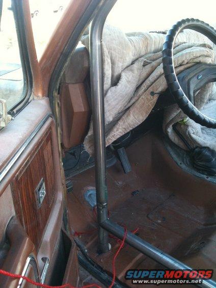 Interior view of a vehicle showing a metal roll cage installed, with a blanket covering the passenger seat and dashboard