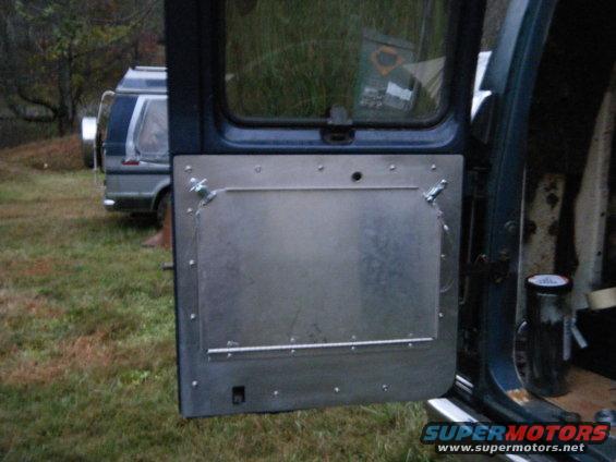 Interior of a van door with a metal panel and a spare tire visible outside