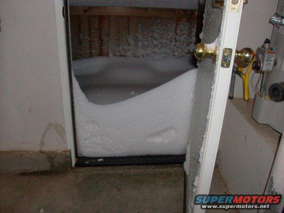 Snowdrift blocking a doorway, with a water heater and pipes visible to the right