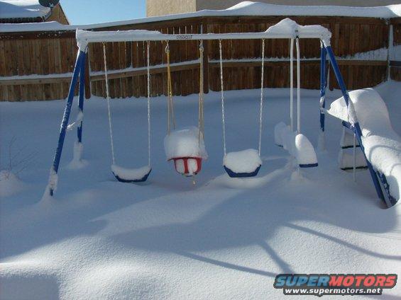 Swing set covered in snow with blue frame and seats