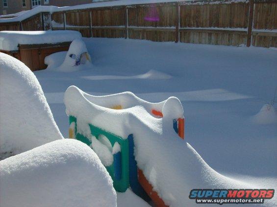 Backyard covered in deep snow, with a colorful plastic slide and mounds of snow obscuring other objects