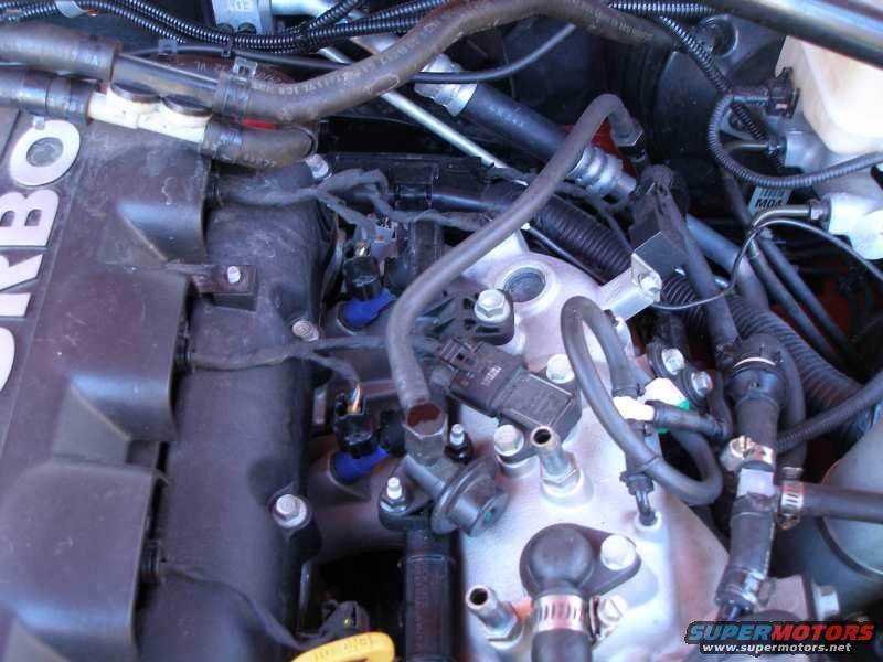 Engine bay with hoses, wires, and fuel injectors. Text 'TURBO' visible on a dark component