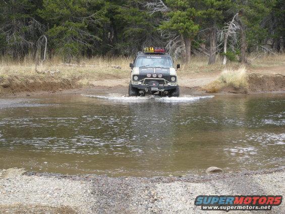 Ford Bronco driving through water, front view. Modified bumper, winch, roof rack