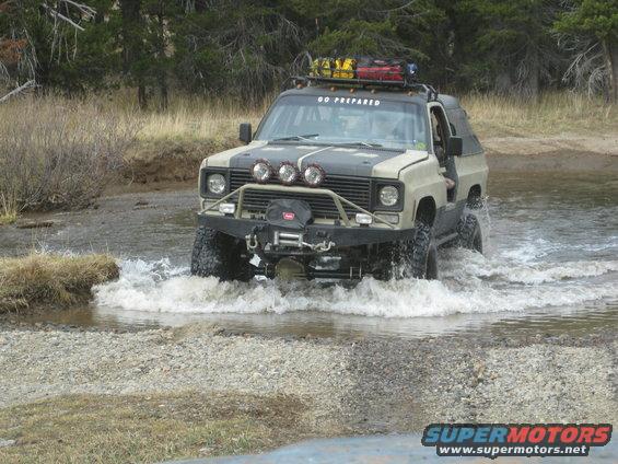 Tan and grey off-road SUV with winch and roof rack driving through water