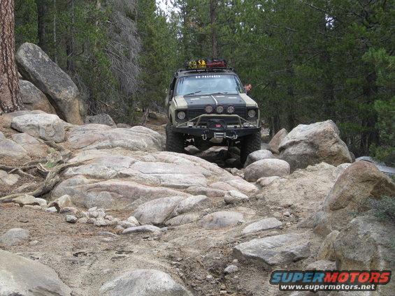 Modified off-road SUV with roof rack and winch driving over large rocks