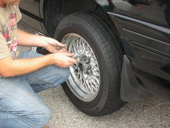 Person in jeans and t-shirt tightening lug nuts on a car wheel