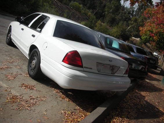 White sedan parked on a dirt lot, rear view. Steel wheels, tinted windows