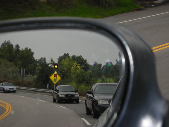 Black sedan seen in side mirror, traffic light ahead