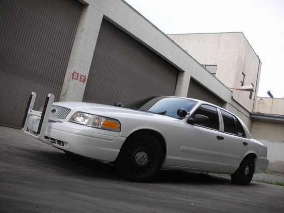 White 2004 Ford Crown Victoria police car parked in front of a garage. It has a push bumper and black steel wheels
