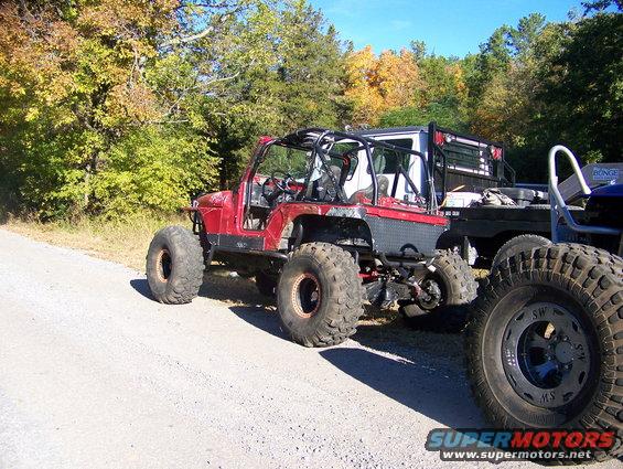 Modified red Jeep with big tires parked next to a flatbed truck
