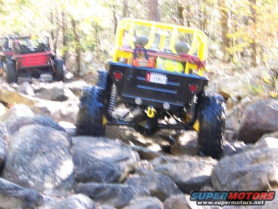 Yellow-caged off-road vehicle with a red one behind it navigating a rocky trail