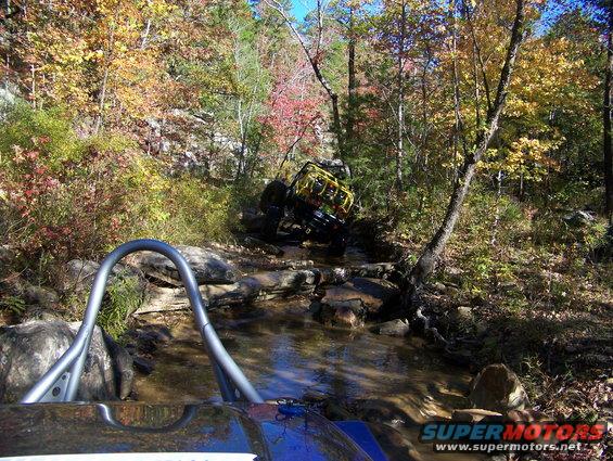 Off-road vehicle in stream, yellow roll cage visible