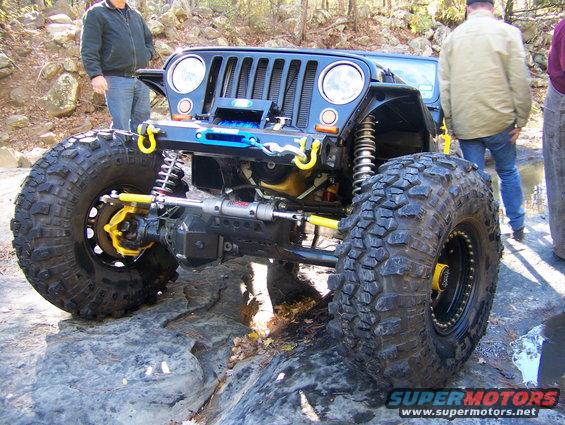 Black Jeep Wrangler with large off-road tires and yellow suspension components on rocks