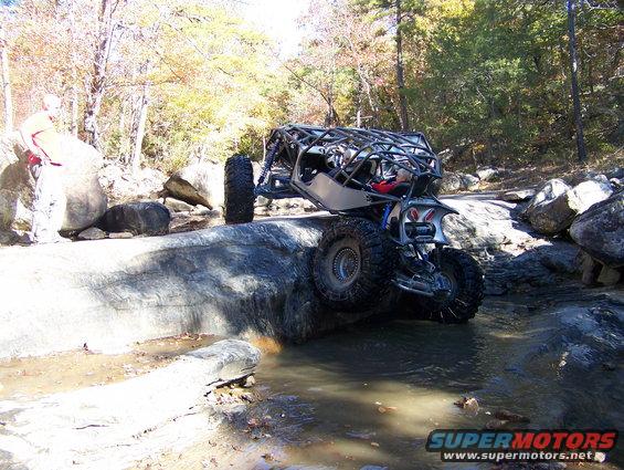 Off-road buggy with roll cage climbing over rocks in a stream