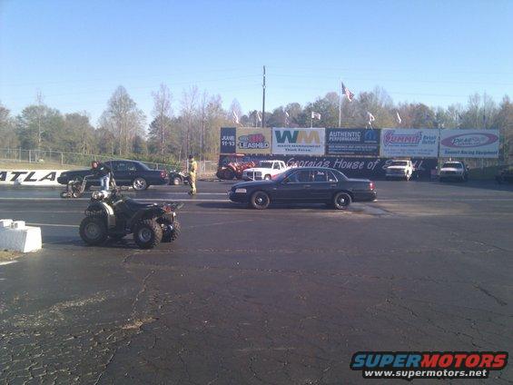 2001 Ford Crown Victoria on drag strip, with ATV in foreground and other cars and people in background