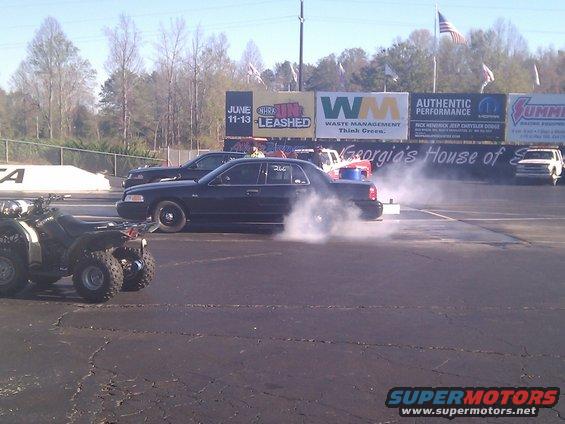 Black 2001 Ford Crown Victoria doing a burnout on a drag strip, side view