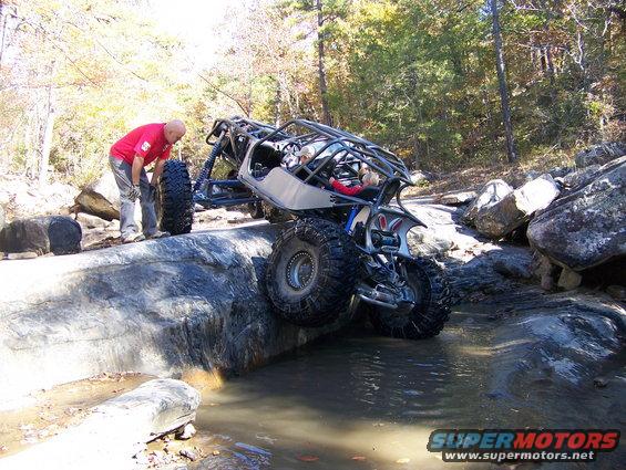 Off-road buggy with roll cage navigating rocky terrain and water