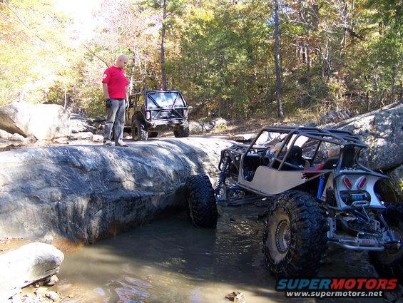 Off-road buggy and Jeep navigating rocky terrain with a person standing nearby