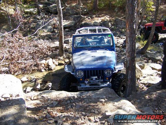 Blue Jeep Wrangler navigating rocky terrain with another red vehicle behind it