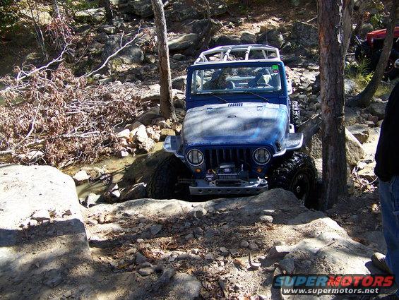 Blue Jeep Wrangler on rocky terrain, front view. Winch installed, roll cage visible