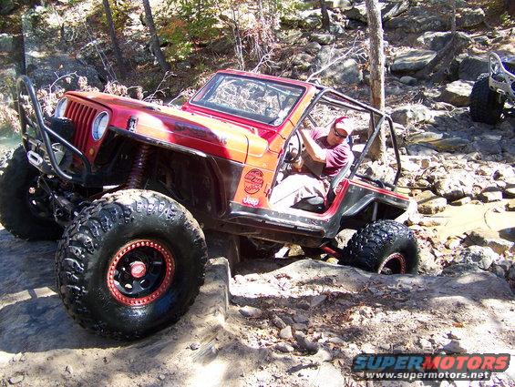 Red Jeep Wrangler navigating rocky terrain with a driver