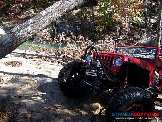 Red off-road Jeep with winch and large tires on rocky terrain near water
