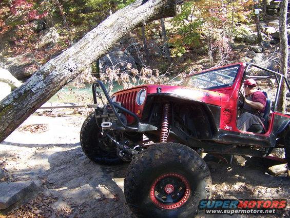 Red Jeep Wrangler with large tires and roll cage on rocky terrain