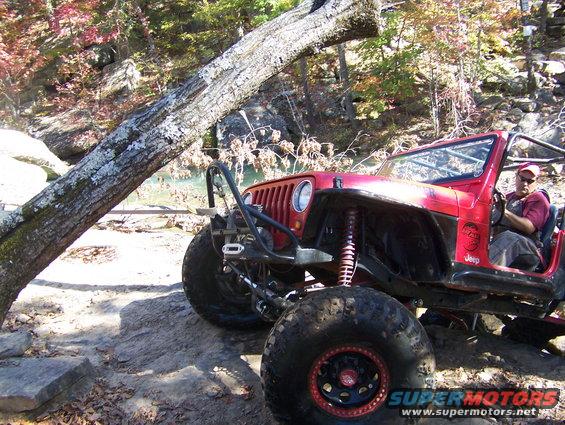 Red off-road Jeep with large tires and roll cage, parked on rocky terrain