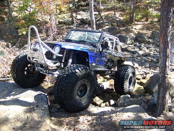 Blue and black off-road Jeep with custom bumper and large tires navigating rocky terrain