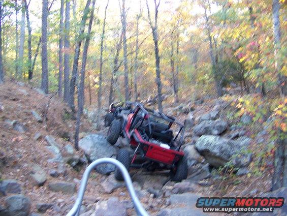 Red off-road vehicle navigating a steep, rocky trail