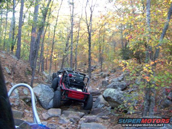 Two off-road vehicles navigating a steep, rocky trail in a forest during autumn