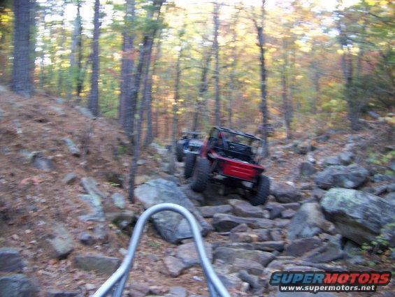 Two off-road vehicles navigating a steep, rocky trail in a wooded area