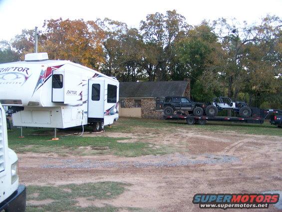 Fifth wheel camper parked next to a trailer carrying a black SUV and a white off-road buggy